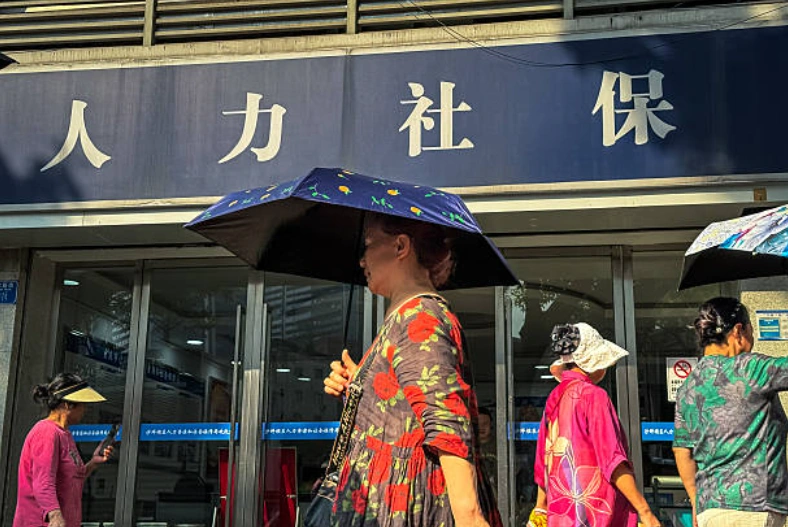 几位老年妇女撑着伞走过重庆市人力资源和社会保障局的办公室门口。 (Photo by Cheng Xin/Getty Images)