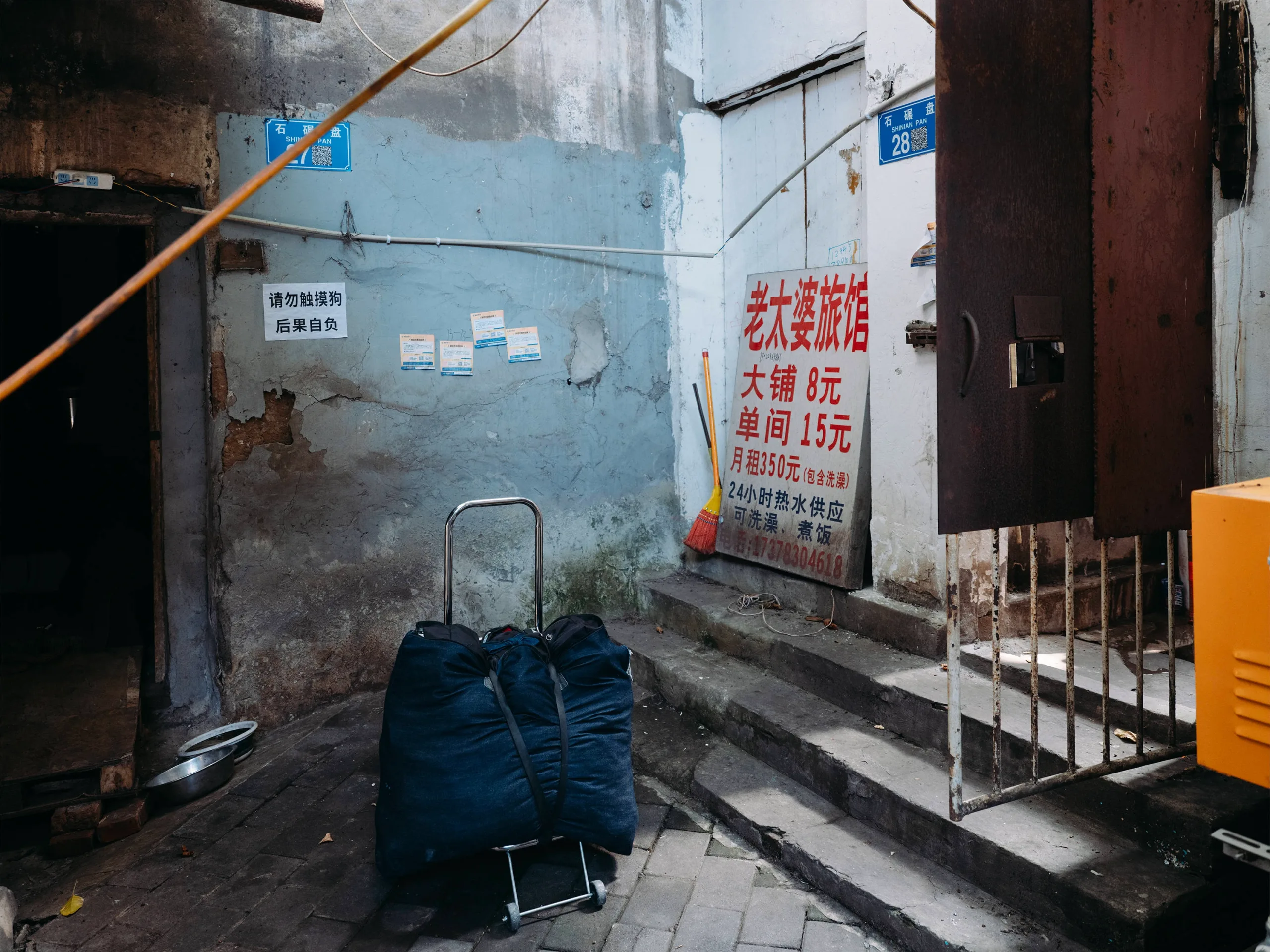 巷子里的旅店招牌。重庆沙坪坝的城中村巷弄里，木牌上写着 “住宿：大铺8元，单间15元”。