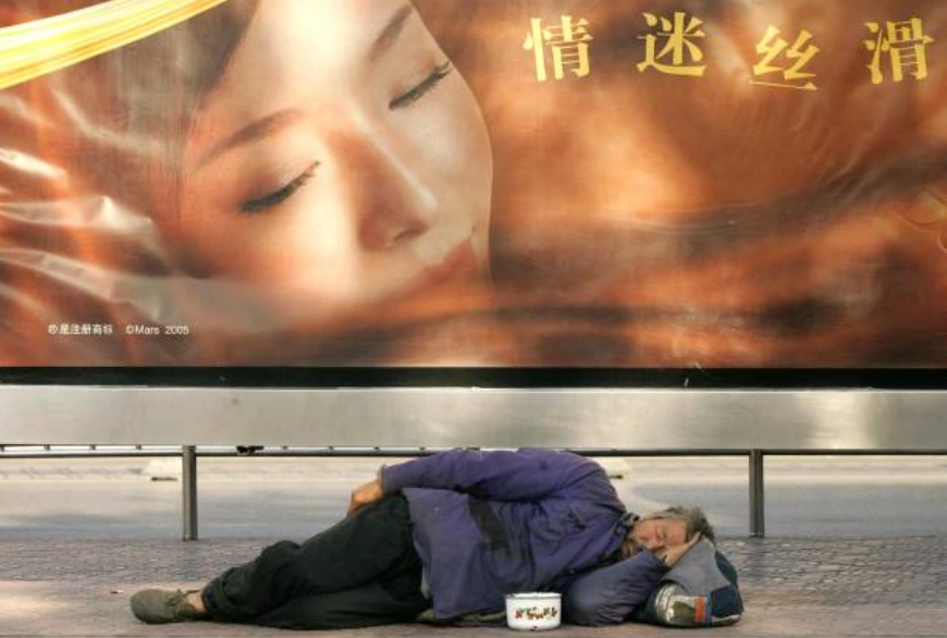 資料圖片：一名無家可歸的男子睡在北京街頭的廣告海報下。(Photo by PETER PARKS / AFP) (Photo by PETER PARKS/AFP via Getty Images)