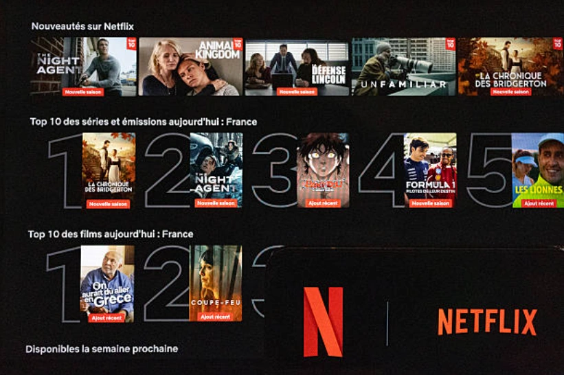一台显示Netflix“N”标志的智能手机被放置在电视机前，电视屏幕上显示着Netflix主屏幕以及“十大热门内容”列表。(Photo by Isabelle Souriment / Hans Lucas / AFP via Getty Images)