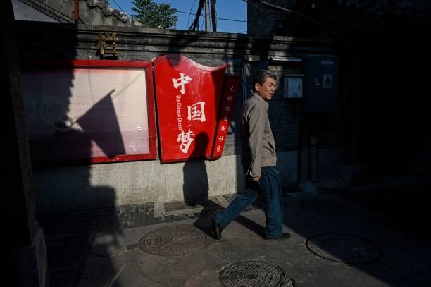 2022 年 10 月 6 日，一名男子在北京的一條胡同裡行經寫有「中國夢」字樣的宣傳欄。（JADE GAO/AFP via Getty Images）